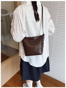 Detail of dark brown woven texture and brand metal plaque on minimalist bucket bag