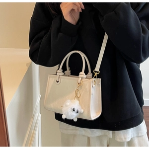 Detail of a creamy white leather handbag with a plush sheep charm and gold hardware