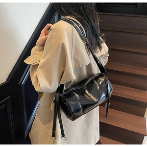 Detail einer schwarzen Lackleder-Zylindertasche mit Metallringen und verstellbarem Riemen