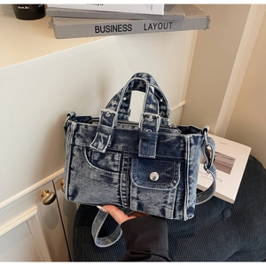 Detail of blue denim handbag featuring a front flap pocket with metal buckle accents