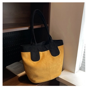 Close-up of yellow suede tote bag with black handles on a wooden bookshelf