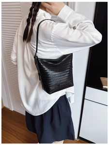 Detail of black woven leather bucket bag featuring adjustable shoulder strap on model