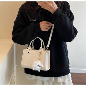 Detail view of cream PU leather handbag featuring dual handles and a plush sheep pendant