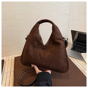 Detail of a dark brown suede triangular handbag with integrated handle and thin strap