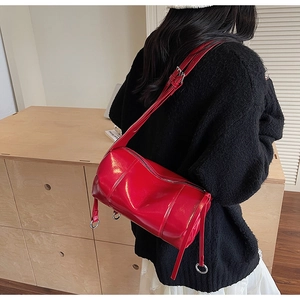 Detail of glossy red cylinder shoulder bag with silver hardware on a female model