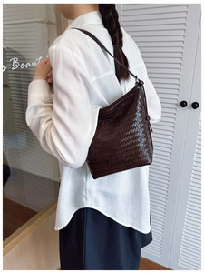 Detail of dark brown woven leather hobo bag with a metallic logo plate and slim strap