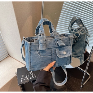 Detail of washed denim tote bag featuring utility pockets and silver buckle accents