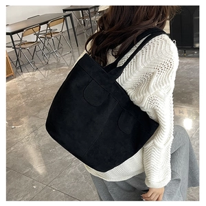 Detail view of a large black tote bag with suede texture shown on the shoulder