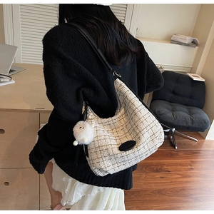 Close-up of beige tweed shoulder bag with black strap and white plush doll pendant