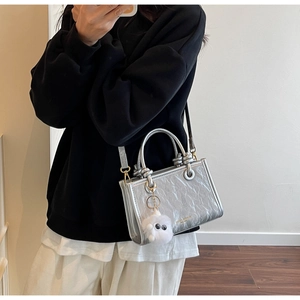 Détail d'un sac cabas argenté plissé avec logo doré et accessoire de charme en peluche