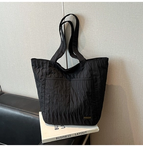 Details der schwarzen Nylon-Einkaufstasche mit Falten, Vordertaschen und Markenlogo-Schild