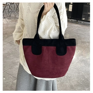 Detail of burgundy suede tote bag with black contrast handles and decorative patches