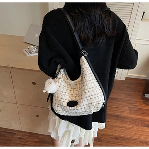 Detail of tweed hobo bag with black leather strap and plush doll charm in lifestyle setting