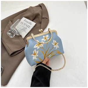 Detail of elegant light blue embroidery handbag with golden floral motifs and chain