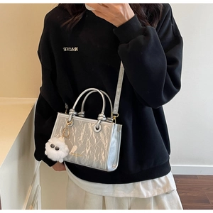 Sac bandoulière argenté plissé avec breloque monstre en peluche porté devant un miroir