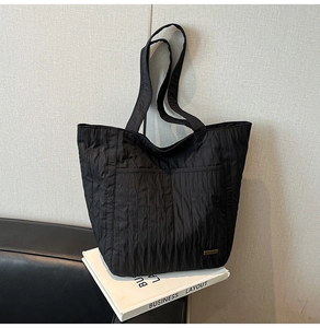 Detailansicht der schwarzen Falten-Tote-Bag mit feinen Nähten und metallischem Logo-Akzent