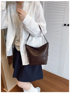 Detailed view of dark brown woven leather bucket bag with brand label and strap