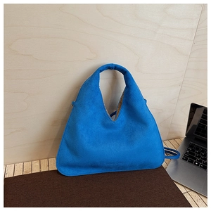 Detail of blue suede dumpling bag showing its matte texture and curved handle design