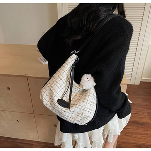 Detail of white tweed hobo bag with black leather strap and fluffy pom-pom charm