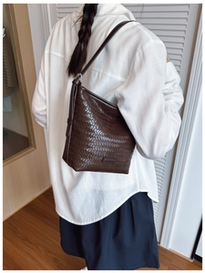 Brown woven leather bucket bag worn as a shoulder bag on a model in home interior