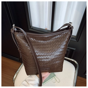 Close-up of dark brown woven leather bucket bag with adjustable strap on white armchair