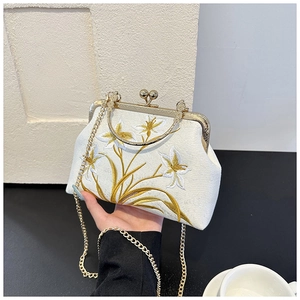 Detailed embroidery on a cream silk handbag with golden handle and vintage clasp