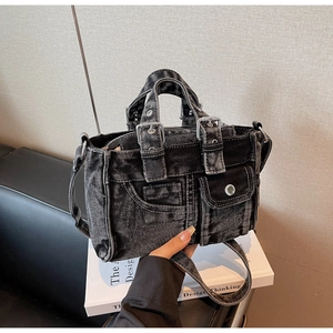 Detail of black denim multi-pocket tote bag showing metal buckles and contrast stitching