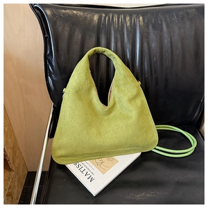 Detail view of avocado green suede dumpling bag on a black leather chair with art book