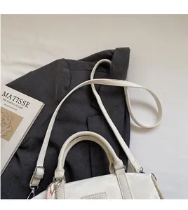 Detail of cream-white pillow bag featuring a metal logo and colorful fabric pendant