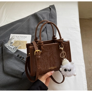 Detail of glossy brown leopard texture bucket bag with plush monster charm and knotted handles