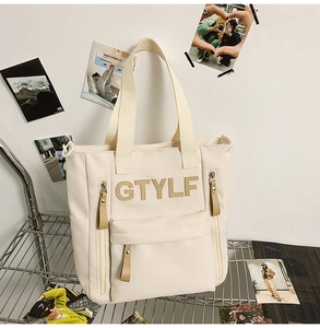 Detail of off-white canvas tote bag featuring textured lettering and leather zipper pulls