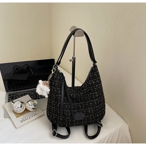 Detail of tweed hobo bag with gold texture and plush sheep charm on a desk