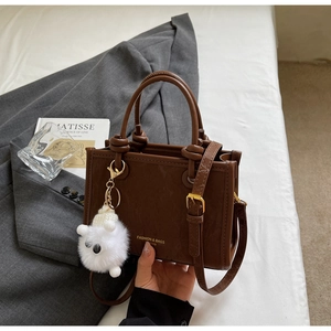 Close-up of dark brown leather bucket bag with knotted handle and plush monster charm