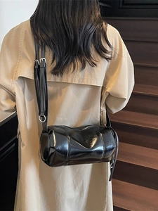 Minimalist black glossy pillow bag with adjustable strap worn with a beige trench coat