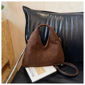 Detail of a dark brown suede crossbody dumpling bag on a stylish leather seat