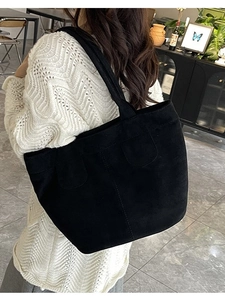 Black minimalist faux suede tote bag with decorative stitching shown on shoulder