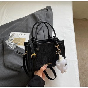Detail of black textured handbag featuring gold lettering and a cute white plush charm