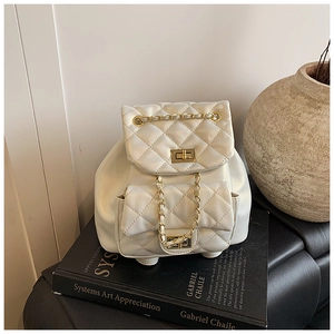 Detailed macro view of white quilted mini backpack with gold chain and twist lock on a book