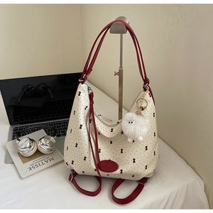 Detailed view of large hobo bag with red trim, bow prints, and a plush ball charm