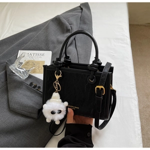 Detail of black leather bucket bag with gold hardware and white plush monster charm accessory