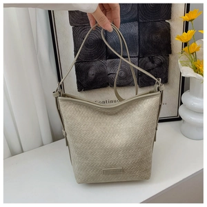 Detail of light grey-green woven bucket bag with leather strap and metal hardware