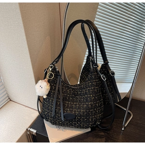 Close-up of black tweed hobo bag with gold threads, leather trim and plush charm