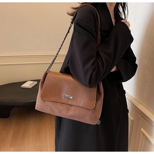 Dettaglio di una borsa sottobraccio vintage marrone con catena dorata e logo in metallo