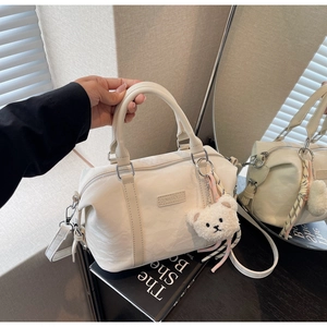 Detail view of cream Boston bag with silver hardware and cute plush bear charm
