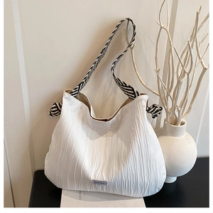 Détail du sac hobo blanc plissé avec bandoulière rayée tissée et étiquette décorative