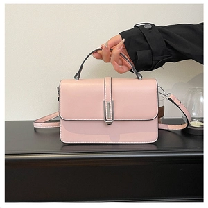 Pink rectangular handbag with silver metal buckle and black handle on black surface