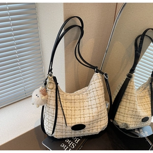 Detail of tweed hobo bag with black leather strap and plush lamb pendant by a mirror