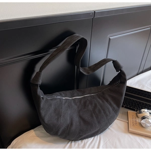 Macro shot of large black quilted canvas croissant bag on bed with urban lifestyle props