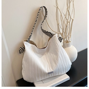 Détail du tissu blanc plissé et de la bandoulière rayée sur le grand sac cabas