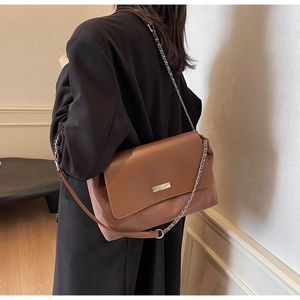 Detail of brown leather and suede mix shoulder bag with silver chain strap worn by a model